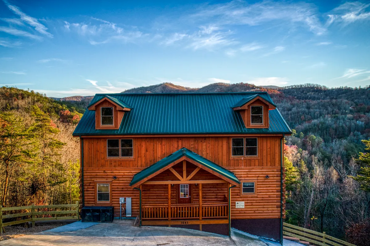 A rustic wooden structure with a green metal roof stands on a porch area, set against a dramatic mountain backdrop. The inviting porch is positioned to offer sunrise views and a peaceful connection to the natural world.