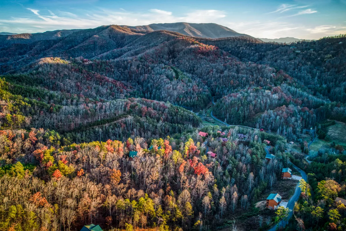 A scenic view showcasing rolling mountains carpeted with brilliant autumn foliage, dotted with scattered cabins and crossed by a winding road. The landscape exudes tranquility and the sense of endless opportunities for hiking, exploration, and immersion in nature.