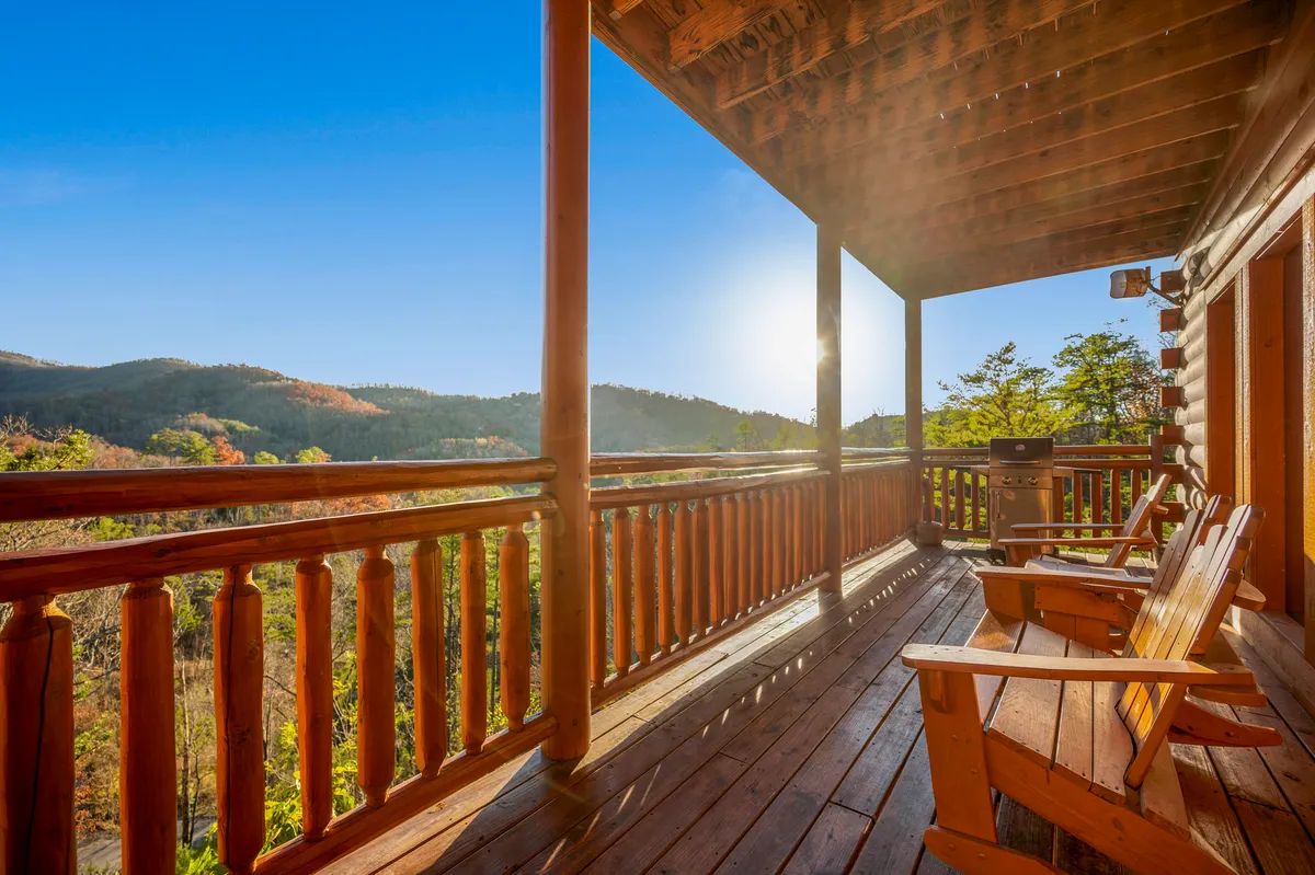 A welcoming exterior wooden deck furnished with classic rocking chairs, all oriented toward panoramic mountain views. Sunlight pours over the scene, suggesting a comfortable, inviting space perfect for relaxing, conversing, or hosting small outdoor gatherings.
