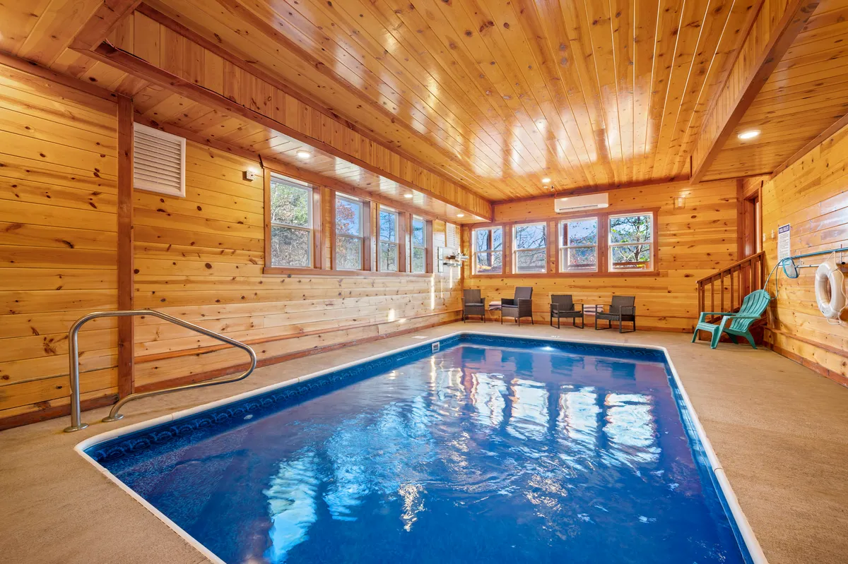 An indoor oasis featuring a sparkling swimming pool set against wood-paneled walls and ceiling, with a seating area nearby. The atmosphere is cozy yet lively, suggesting opportunities for both relaxation and vibrant group gatherings.