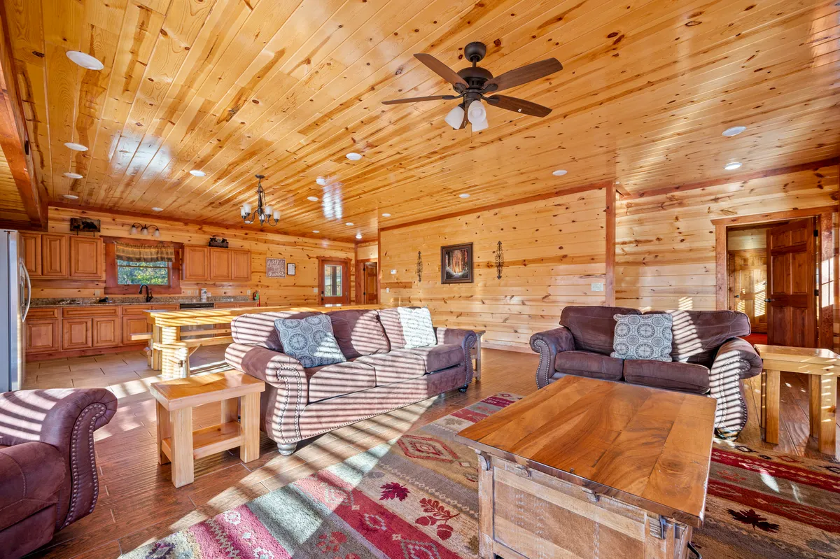 A warm, inviting living room with comfortable sofas, a rustic wooden coffee table, a colorful area rug, and a wooden ceiling. The room is set up for family gatherings, with plenty of space for games and relaxation.