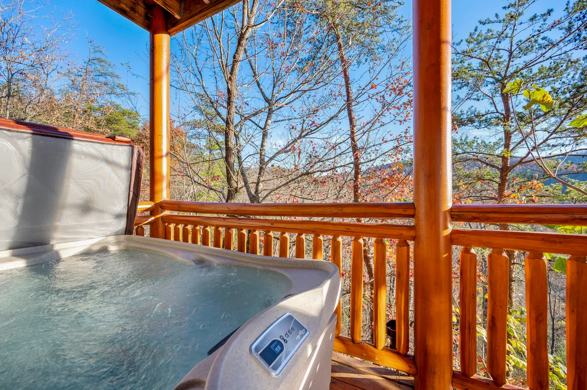 An inviting outdoor hot tub sits nestled against a wooden railing, surrounded by trees and natural scenery. The tranquil setup is ideal for relaxing soaks under the stars, offering a serene post-adventure retreat.