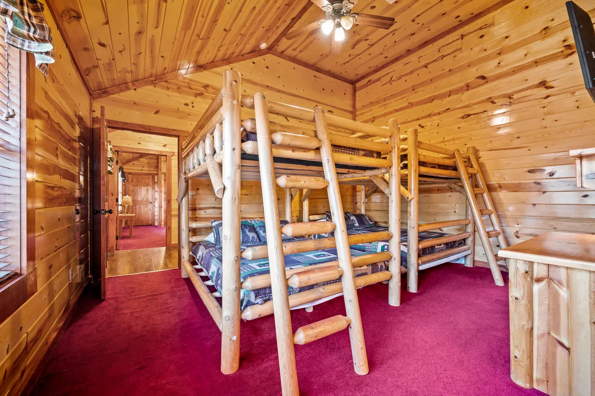 A welcoming bunk room with sturdy wooden bunk beds, soft carpeted flooring, and a rustic wooden interior. The space is ideal for kids to play, tell stories, or enjoy restful sleep after a day of adventure.