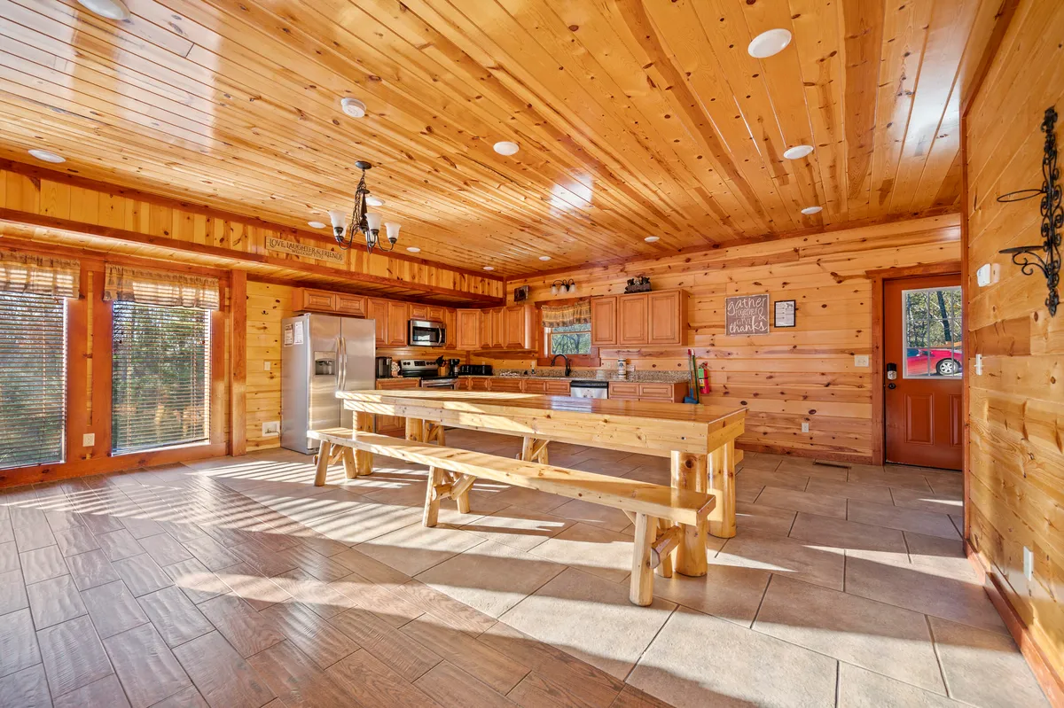 A warm, inviting kitchen and dining area featuring a large wooden table, modern kitchen appliances, and expansive windows that fill the space with natural light. The setup emphasizes a communal atmosphere perfect for family gatherings or festive meals.
