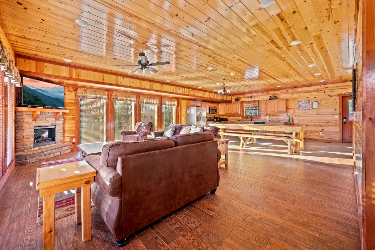 An open-concept living and dining area that features a cozy fireplace, large windows framing the mountains, a generous dining table, and a plush sofa. The room is bathed in warm light, encouraging relaxation and shared meals.