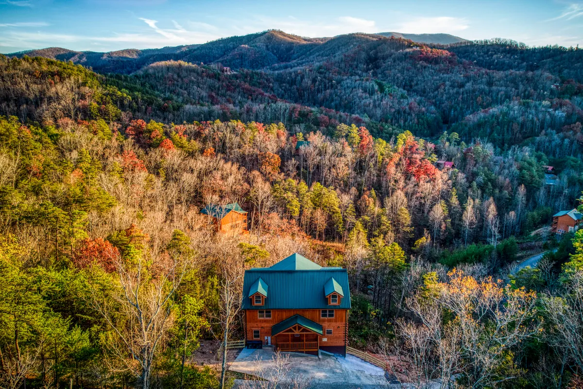 A large wooden house sits nestled among surrounding mountains and a dense forest, highlighting the natural grandeur and seclusion of the Smokies. The structure’s spacious design and elevated position offer sweeping mountain views, suggesting the luxurious feel of a private lodge retreat.