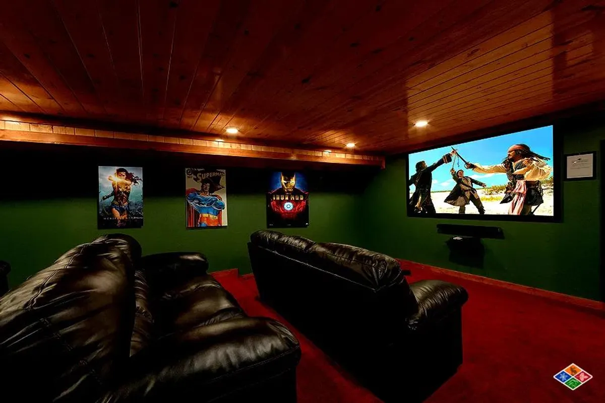 A dedicated home theater room with black leather couches arranged for optimal viewing, a large screen TV dominating the wall, and classic movie posters adding cinematic flair. The room invites guests to settle in for immersive movie nights or gaming sessions.